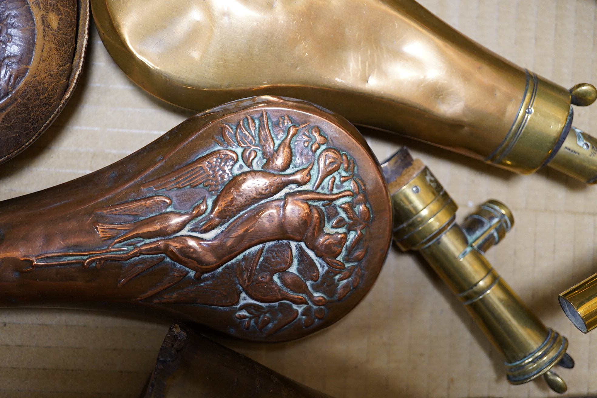 Four assorted copper powder flasks comprising; a three-way flask by Sykes (dented), ‘three horses head’ flask by Hawksley and two others, together with two leather shot flasks, a horn powder flask and a percussion nipple